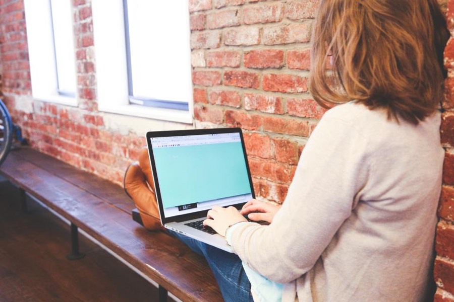A person working at a laptop on a long desk beside a window.