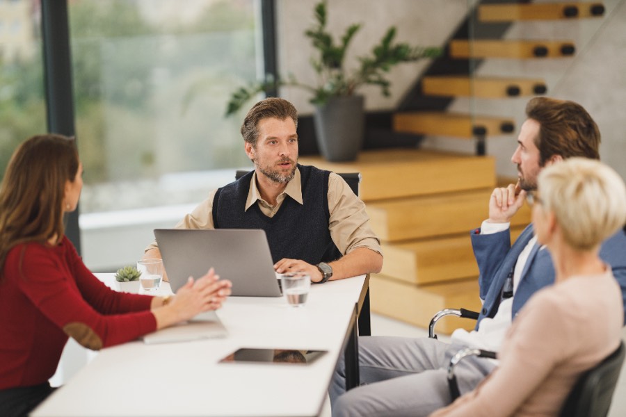 Colleagues around a meeting table with a laptop, mid-discussion.